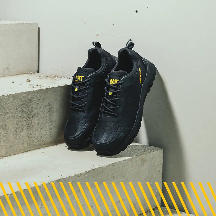 A pair of Caterpillar Inductor Mesh Low Safety Trainers in black propped up against a wall on concrete steps.
