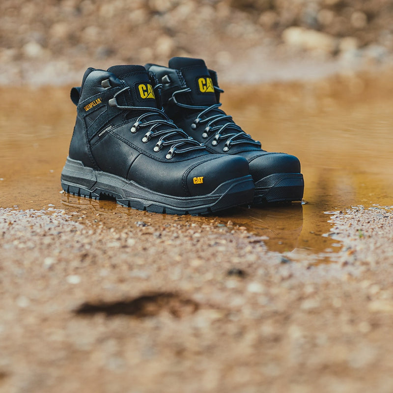 Pair of black Caterpillar Pneumatic 2.0 Safety Boots on a wet, muddy work site