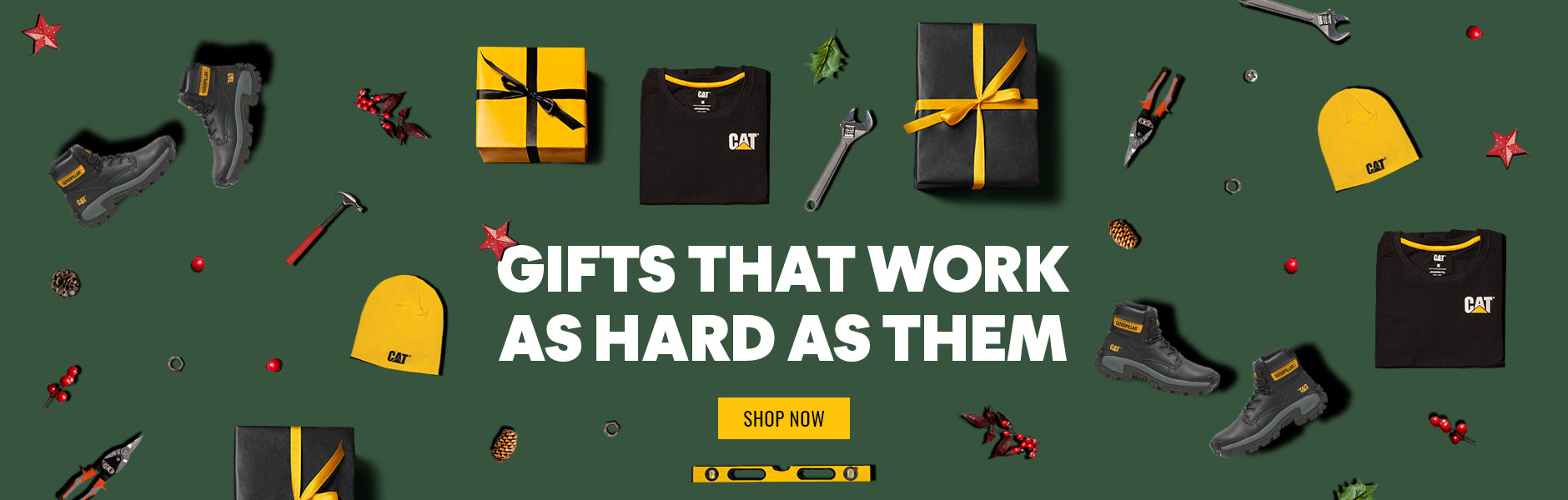 A selection of Caterpillar workwear, footwear, Christmas decorations and work tools laid out on a green background