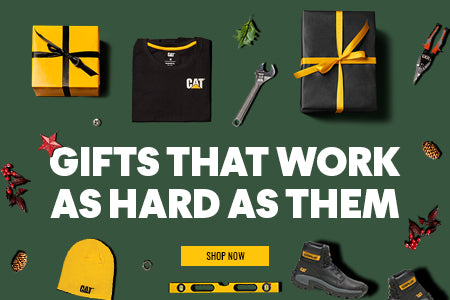 A selection of Caterpillar workwear, footwear, Christmas decorations and work tools laid out on a green background